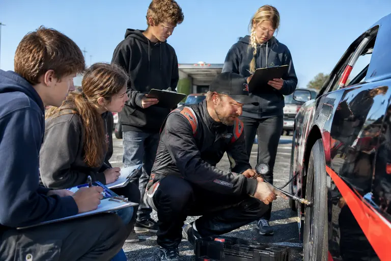 Amateur racing helpers checking tools, tires, and food beside a trailer